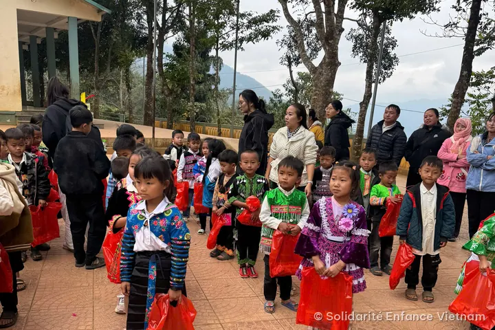 Des enfants en costumes traditionnels, chacun avec un sac rouge, dans la cour de l’école.