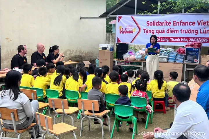 Remise de cadeaux à l’école de Lũng Cao : des enfants en polo jaune assis devant une banderole de l’association.