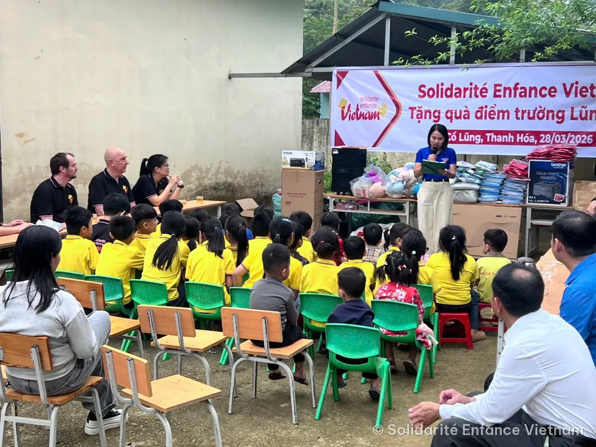 Remise de cadeaux à l’école de Lũng Cao : des enfants en polo jaune assis devant une banderole de l’association.