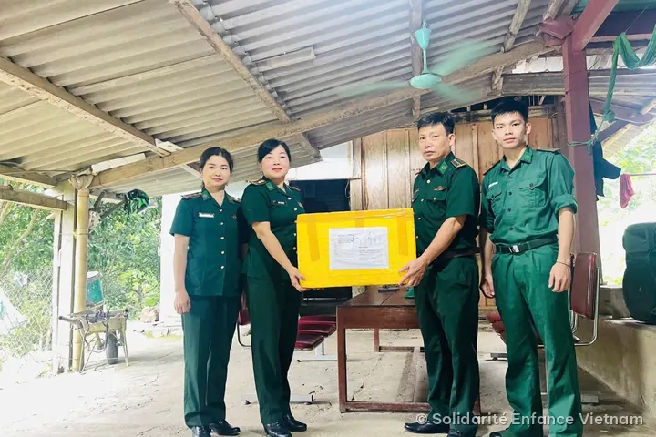 Remise d’un carton de médicaments à des personnes en uniforme vert, sous un auvent.
